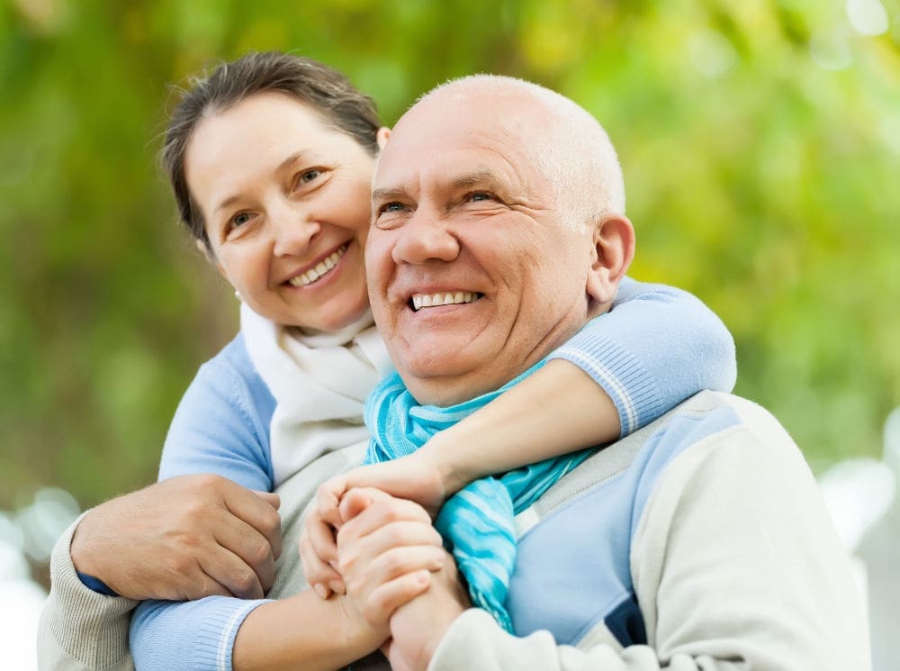 Man and woman embracing and smiling outdoors with dental implants in Lexington