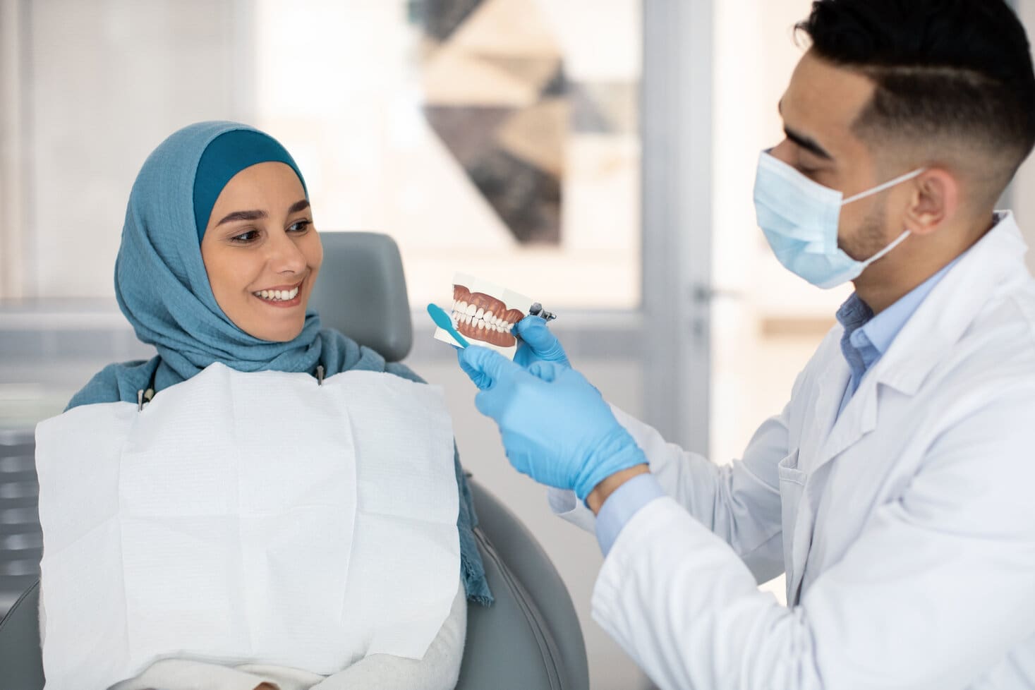 Dentist brushing a model of the teeth next to smiling woman in dental chair