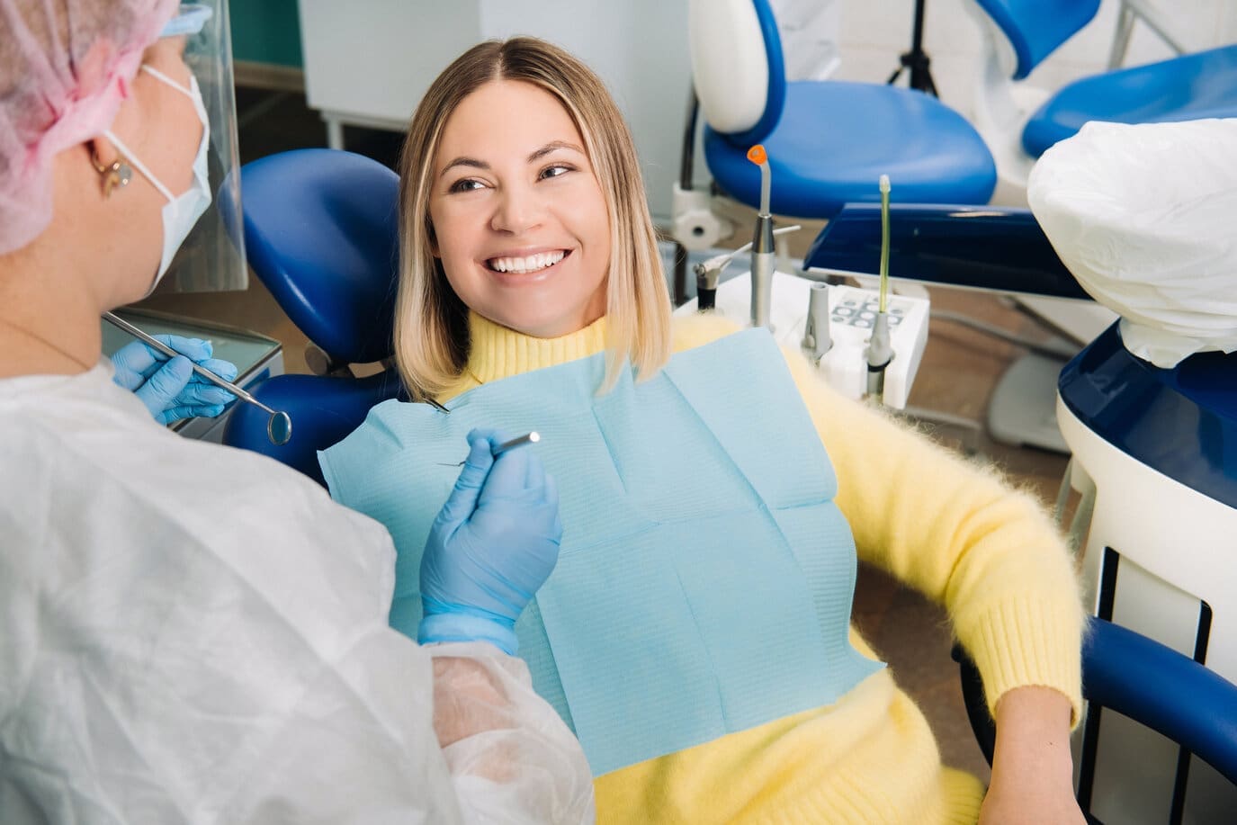 Woman in yellow sweater smiling at her dentist during a dental cleaning