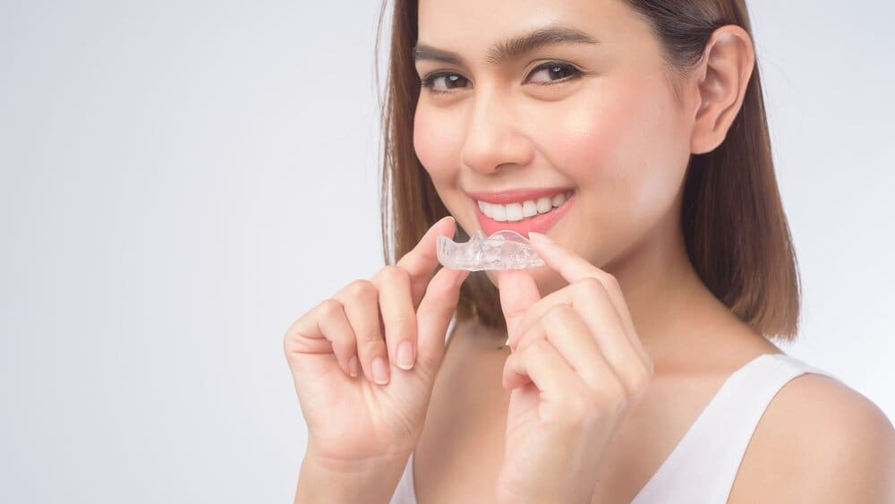 Young smiling woman holding invisalign braces over white background studio, dental healthcare and Orthodontic concept.