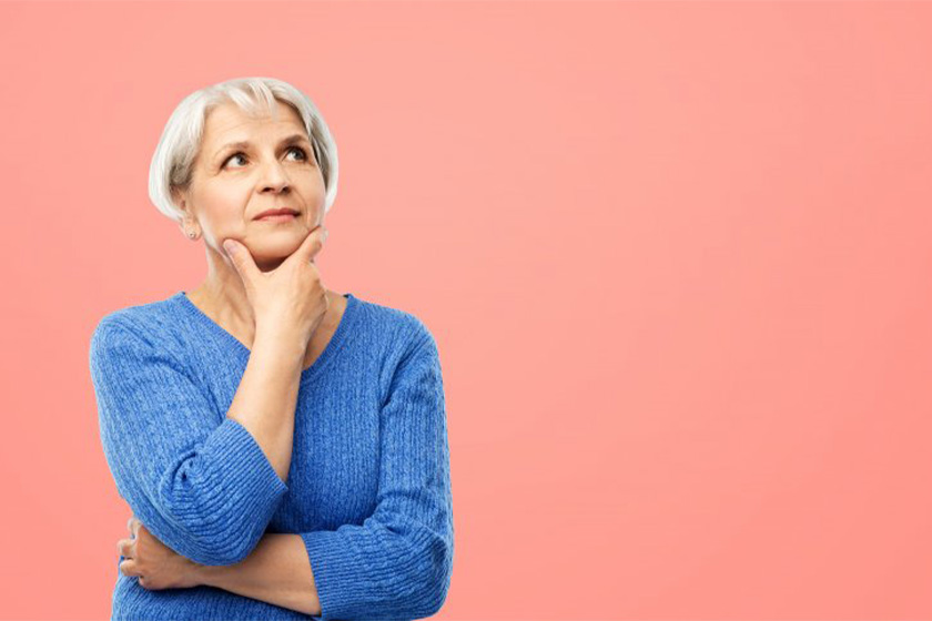 An older woman stands thoughtfully with her hand on her chin, gazing into the distance.