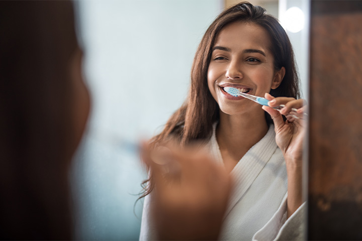 A woman brushing her teeth in front of a bathroom mirror