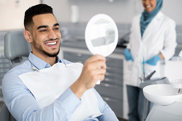Man smiling at reflection in handheld mirror