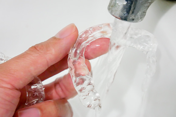 Patient rinsing clear aligner with water in sink