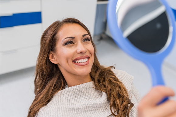 Woman smiling at reflection in handheld mirror