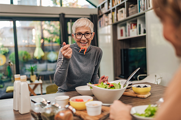Woman smiling while eating lunch with friend in kitchen