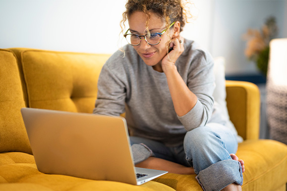 Woman with glasses smiling while looking at laptop