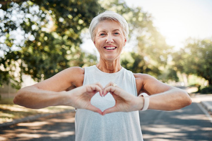 Smiling lady makes shape of heart with her hands.