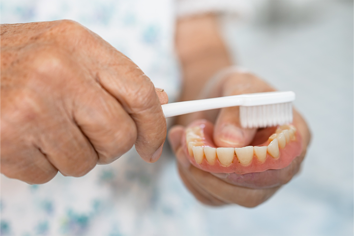 A patient cleaning their denture with a toothbrush.