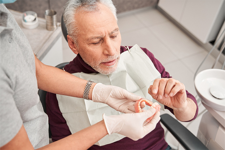 A patient looking closely at dentures held by a dentist.