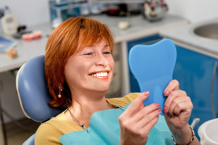 A senior woman in a dentist’s office admiring her new dentures.