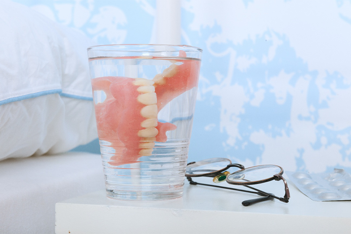 Dentures in a glass that’s sitting on a nightstand.